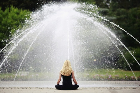 Junge Frau meditiert im Lotussitz vor Springbrunnen