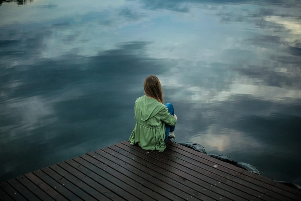 Frau sitzt auf einem Steg und schaut aufs Wasser